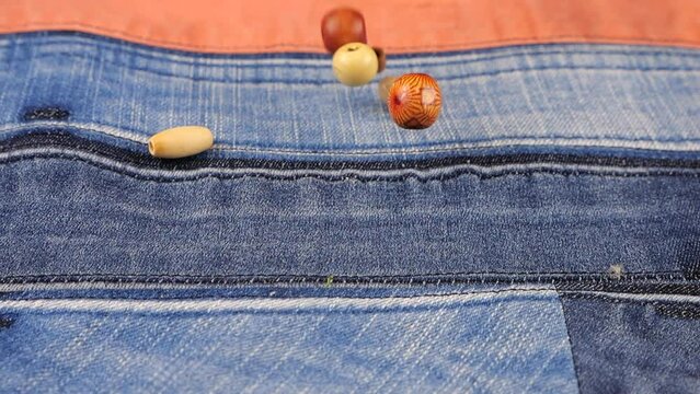 Decor elements made of natural materials, wood and shell beads fall on denim. Slow motion.