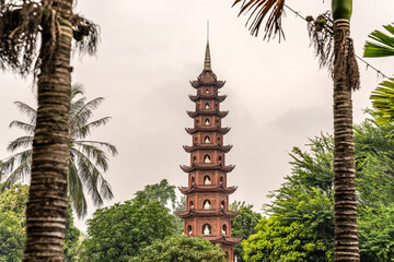 View of the famous Tran Quoc Pagoda in Hanoi, Vietnam, between two palm trees defocused in the foreground as a frame.