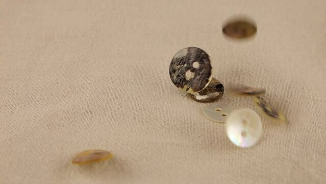 Natural mother of pearl buttons fall on beige natural linen fabric. Slow motion.