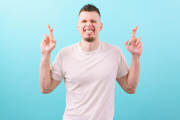 Man with fingers crossed and screwed up face standing against blue background. Stress. Success....