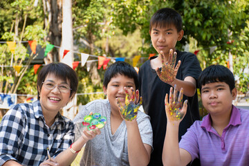 Group of young asian boys show their fingerprint which dirty with watercolor after finishing learning outdoor watercolor painting with their female teacher, soft focus, raising teens concept.