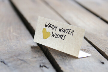 Warm winter wishes. The inscription on the tag on a wooden background.