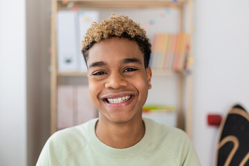 Portrait of smiling young latin american teenage boy looking at camera indoors. POV screen view of...