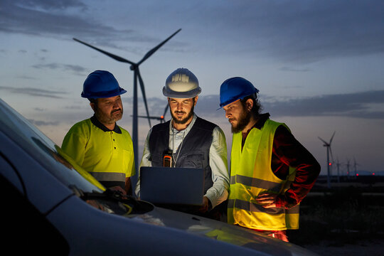 Group of engineers in discussed the plan for the maintenance of wind turbines working with a laptop in a field wind turbines power station. Renewable and clean energy concept, sustainable future