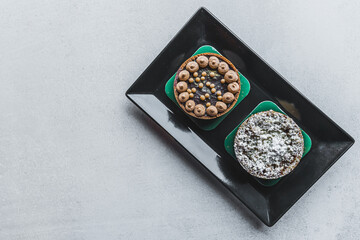 Two tasty tarts lying on black plate on gray table. Art confectionery. High angle view. Copy space. High quality photo