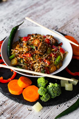 Wok, noodles, udon with pork and pineapple, on black plate and a wooden white background