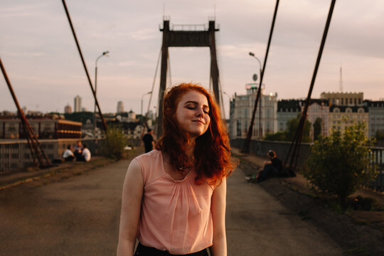 Happy girl with red hair standing on bridge in city
