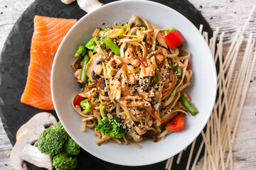 Wok, noodles, udon with salmon, on black plate and a wooden white background top view