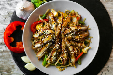 Wok, noodles, udon with eel, on black plate and a wooden white background top view