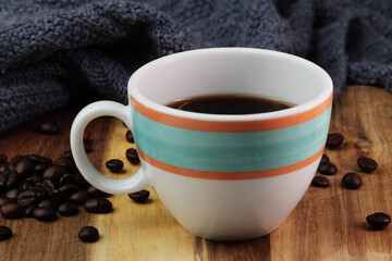 Colorful cup of black coffee is placed on a wooden surface. The beautiful cup with a handle is white with orange and aqua colored rings drawn on them. The surface has an authentic wooden texture.