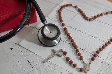 A stethoscope next to a crucifix over an electrocardiogram and a bible