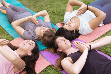 Group of caucasian female friends practicing yoga outdoors. They are lying on the grass in relaxing posture.