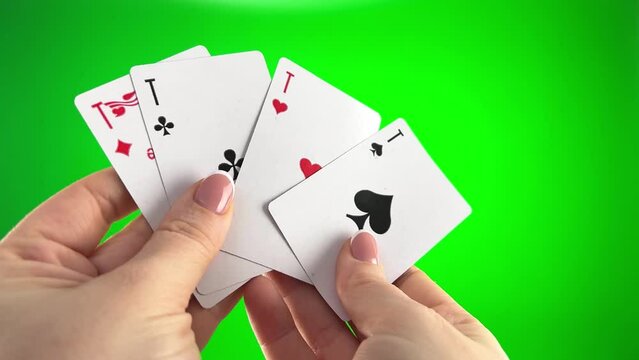 Hand holding four aces on a green background close-up female hands with french manicure. woman sorts through cards, examines them folds and spreads out like fan four cards left of same suit
