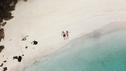 Fototapeta na wymiar Happy couple lying on the tropical beach in Thailand, relaxing, celebrating honeymoon. Turquoise mint color clear water. Drone aerial view from above