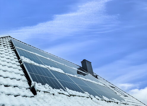Solar panels producing clean energy on a snow coevered roof of a residential house.