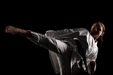 Young girl exercising karate. Child in kimono against black background.