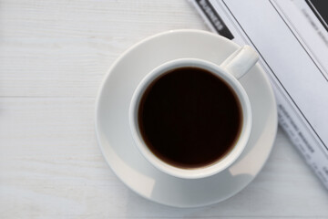 White cup with coffee and newspaper on wooden table in morning, flat lay
