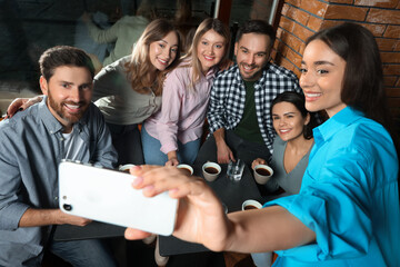 Pretty woman taking selfie with her friends in cafe