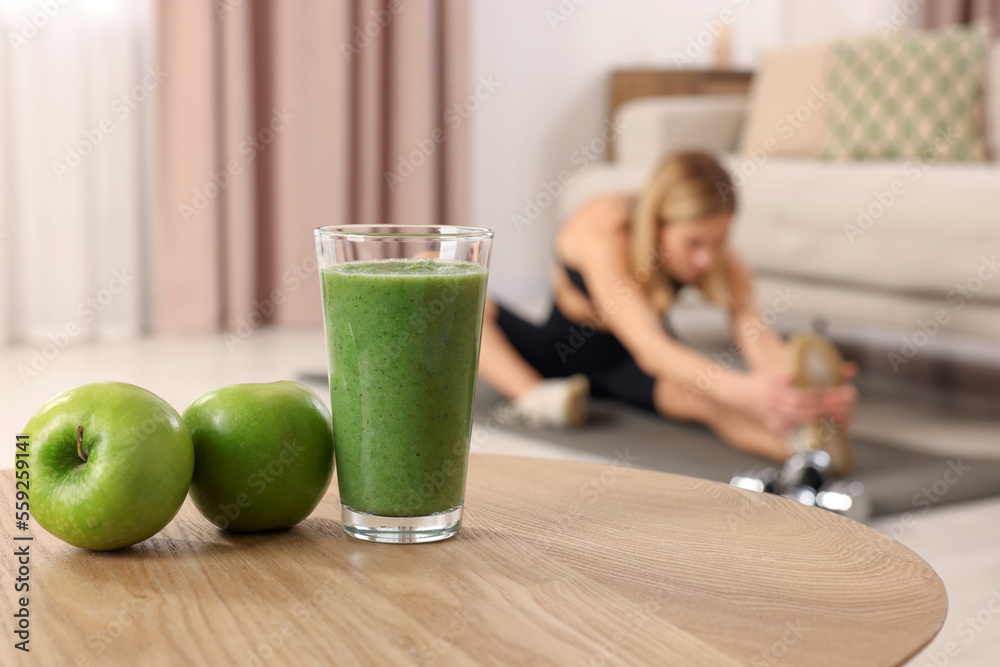 Canvas Prints Young woman in fitness clothes doing exercise at home, focus on glass of smoothie and apples