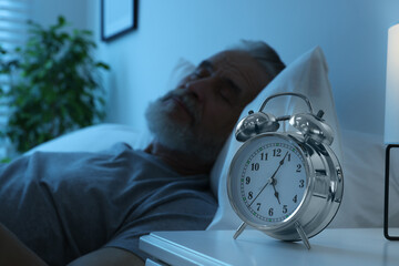 Senior man sleeping in bed at home, focus on alarm clock. Space for text