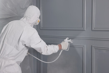 Decorator dyeing wall in grey color with spray paint, space for text