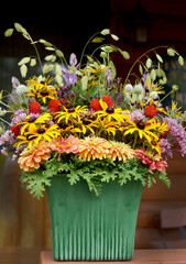 A colorful arrangement of fresh, late-summer garden flowers, foliage, and grasses in a green ceramic container