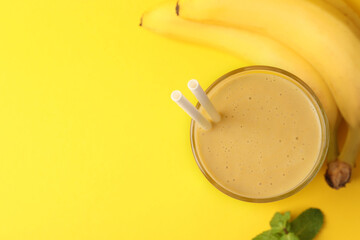 Glass of tasty banana smoothie with straws, fresh fruits and mint on yellow background, flat lay. Space for text