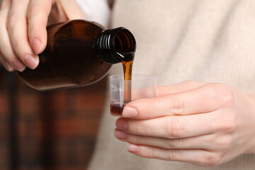 Woman pouring syrup from bottle into measuring cup, closeup. Cold medicine