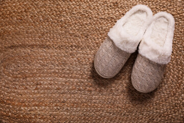 Fototapeta na wymiar Pair of warm stylish slippers on wicker carpet, top view. Space for text