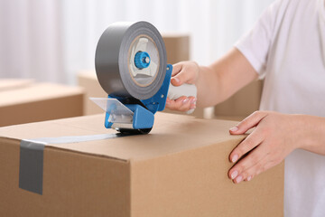Woman applying adhesive tape on box with dispenser indoors, closeup - obrazy, fototapety, plakaty
