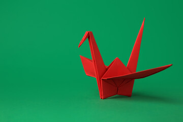 Red paper origami crane on green background, space for text