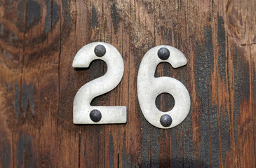 Silver-gray metal numbers two and six (twenty six, 26) nailed to a weathered wood background