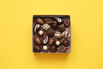 Box of delicious chocolate candies on yellow background, top view