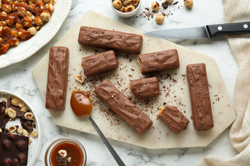 Tasty chocolate bars with caramel and nuts on white marble table, flat lay