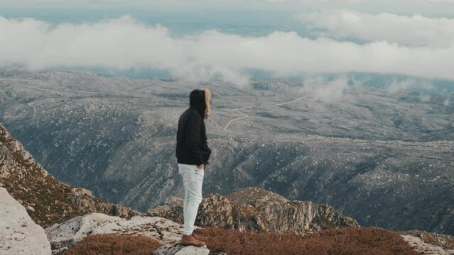 Man standing on a rock and enjoying the magnificent landscape of mountains and clouds with fog. Wide shot with the male out of focus and the landscape in focus. Perfect for travel and adventure themes