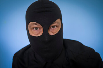 man wearing black shirt and black balaclava against blue background, highjacker, terrorist, robber,...