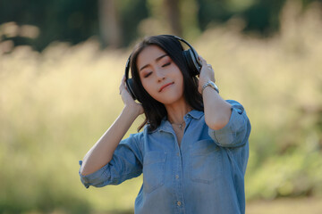 asian woman wearing blue jeans stand and listen to music bluetooth headphone in the garden vetiver flowers against natural light late morning