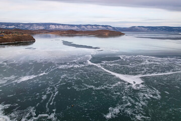 Frozen Lake Baikal, aerial view. Cloudy stormy sky, clear ice in the cracks. Winter landscape.
