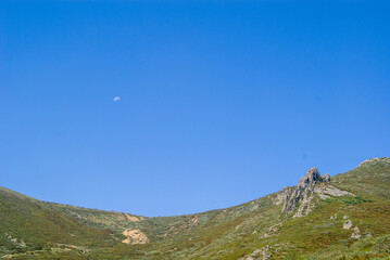 Paisaje montañoso con cielo azul y luna diurna