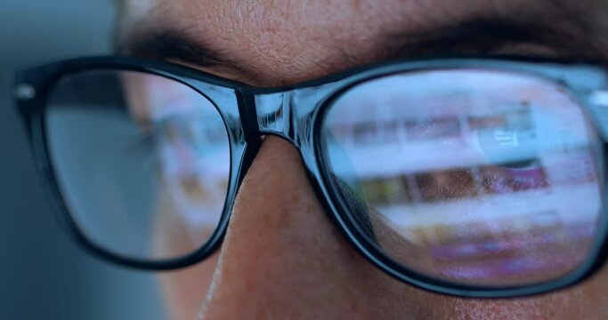 Computer Screen Reflection On Glasses of male internet user searching information on websites at night. Closeup male eyes in glasses scroll internet websites, monitor screen reflect searching pictures