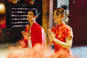Obraz premium Happy young Asian couple in Chinese traditional dresses praying at temple