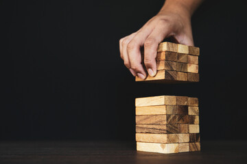 Hand placing wooden block tower stack in pyramid stair step with caution to prevent collapse or...