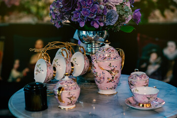 A beautiful set of teapots and teacups placed near the vase of flowers.