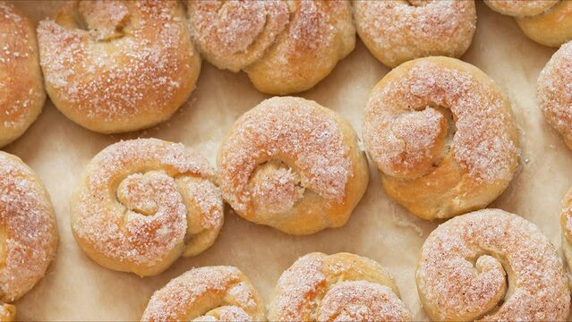 Appetizing hot fresh homemade buns in the form of snails on baking sheet. Delicious sweet snack. Culinary recipe.  Edible background. Top view, close-up, flat lay. Movement with rotation 