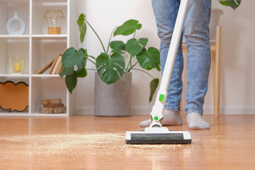 Cleaning room with modern wireless vacuum cleaner without cord. A man in jeans vacuums sawdust from...