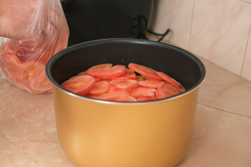 A man puts frozen tomatoes cut into thin slices in a bowl of a slow cooker. Fast cooking. Cooking lunch dinner for family at home. process of cooking meat in French with potatoes, tomatoes, cheese.