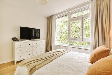 a bedroom with a bed, dresser and tv on the wall in front of the window looking out to the trees...