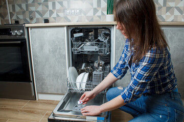 The girl uses the dishwasher. the girl loads the tablet into the dishwasher. Use of a dishwasher. Wash dishes in the dishwasher.