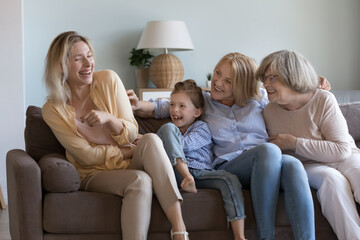 Cheerful happy girls and women of four different generations having fun at home together, tickling,...