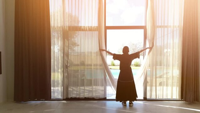 Woman in black dress opens curtains at luxury villa